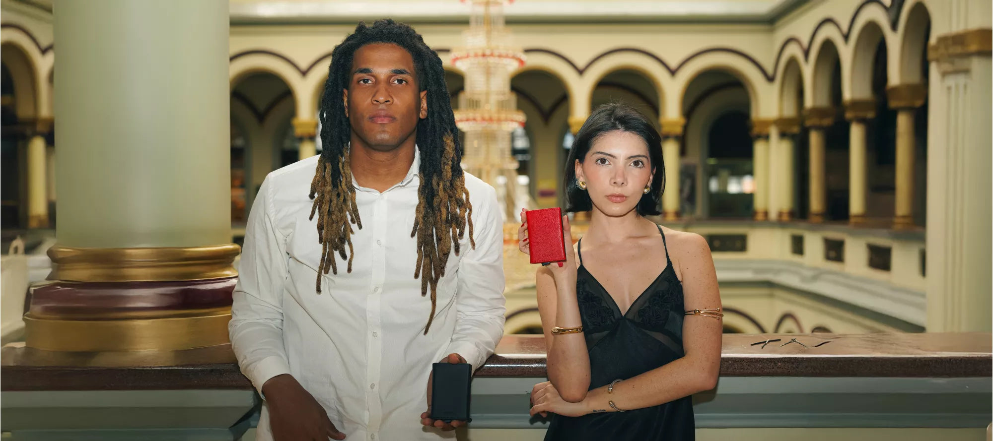 Pareja sonriente tomándose una selfie al aire libre con un iPhone que tiene una billetera magnética anticlonación Urzus adherida en la parte trasera. El hombre sostiene el teléfono mientras la mujer se inclina hacia él. Ambos visten ropa clara y están rodeados de naturaleza con árboles verdes en el fondo.